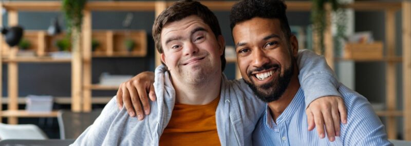 man with down syndrome smiling and hugging another smiling man