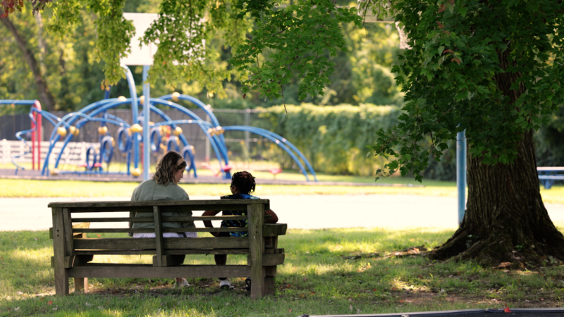 UofL Health - Peace Hospital work is pictured here. A UofL Health worker is sitting on a bench with a local JCPS student near a playground.